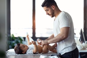 Concentrated young father changing the diapers to his little baby